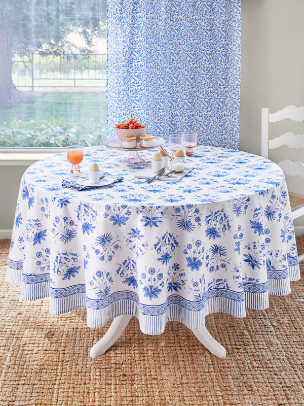 a round blue and white tablecloth with a floral pattern holds egg cups and spring decor at the spring table setting