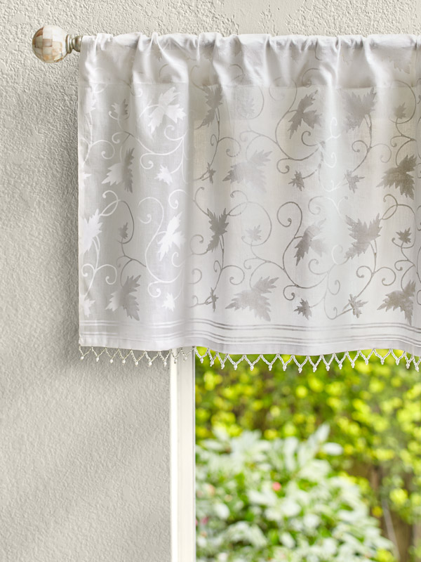 White patterned valance with beading tops a sunny window.