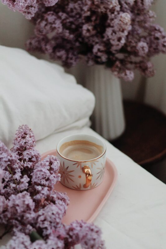 romantic bedding and room with lilac and flowers and cup of tea on a tray