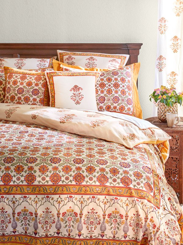 A cheerful bedroom with an orange, cream, sage, and purple vintage duvet cover and pillows based on Persian floral bedding