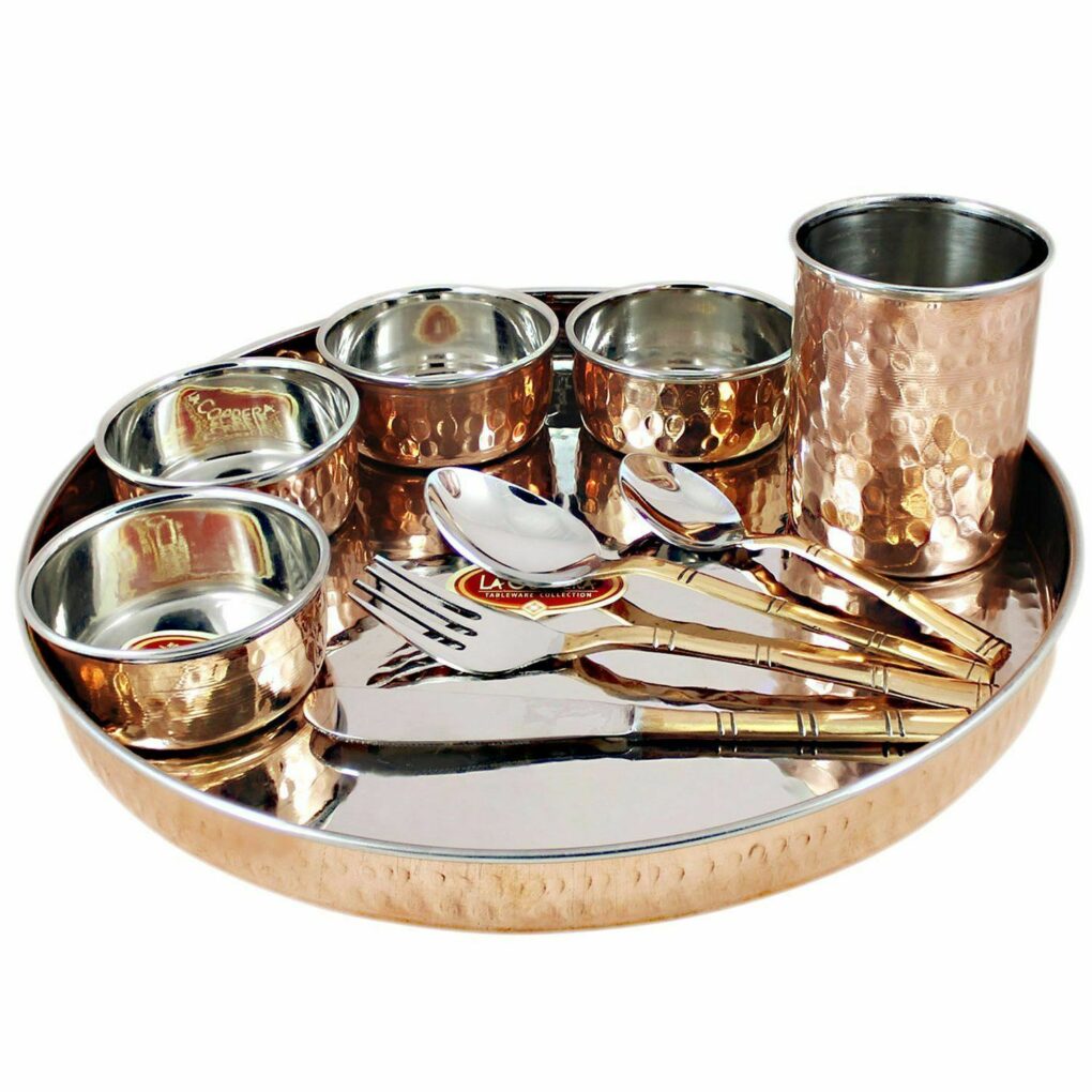 A stainless steel and copper-covered Indian dinnerware set with a serving tray, four bowls, a cup, and flatware