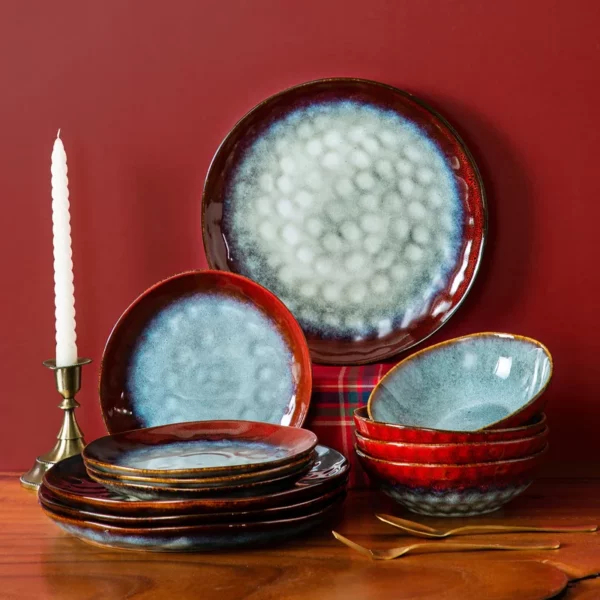 A ruby red dinnerware set with turquoise centers set against a red backdrop next to a candle holder and white candle