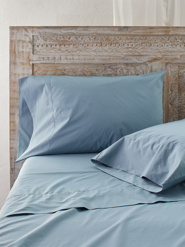 Photograph of light blue bedsheet and pillows with a brown headboard
