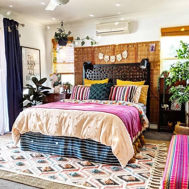 A bedroom with a large bed with a wooden and wicker headboard and colorful throw pillows and blankets on top