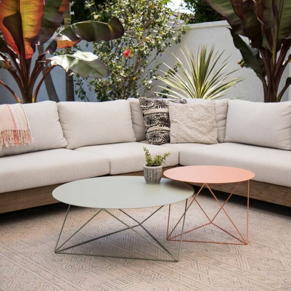 A patio with sage green and pink tables in the foreground and an off-white L sofa in the background