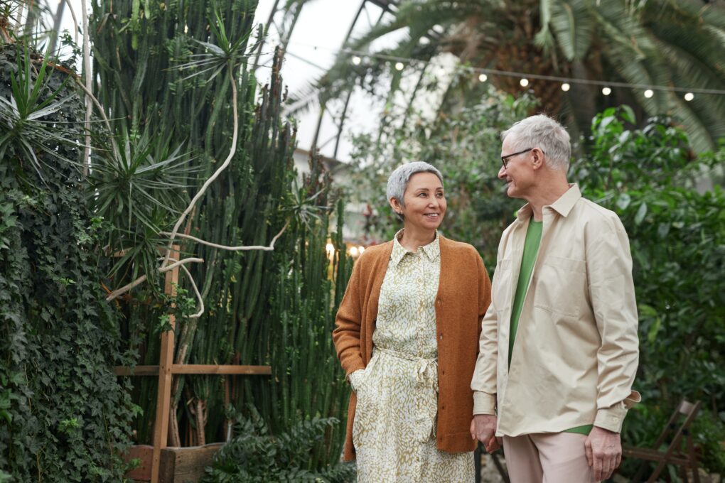 Photograph of an older couple in a greenhouse holding hands and smiling at each other