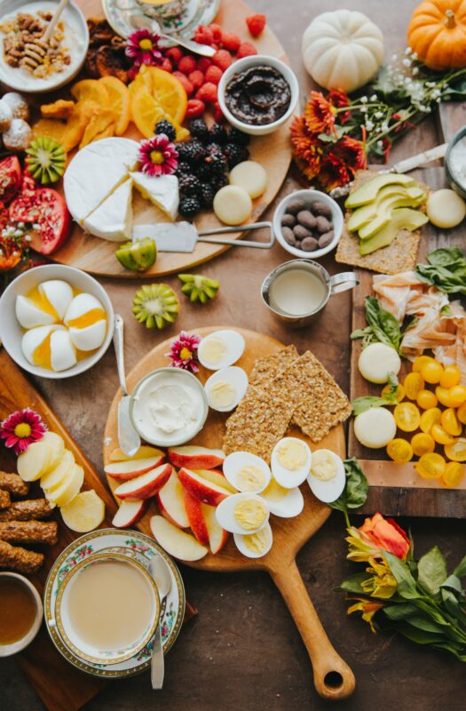 Photograph of a floral-theme charcuterie board with finger foods like cut eggs, apples, biscuits, and fruit.
