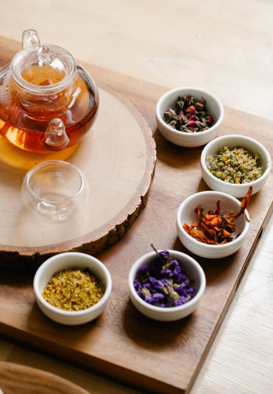 Photograph of tea ingredients in ramekins and a teapot set on a wooden serving tray