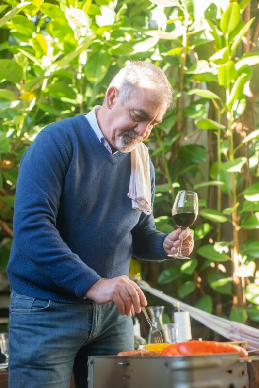 Photograph of man grilling outside with a wine glass in hand 