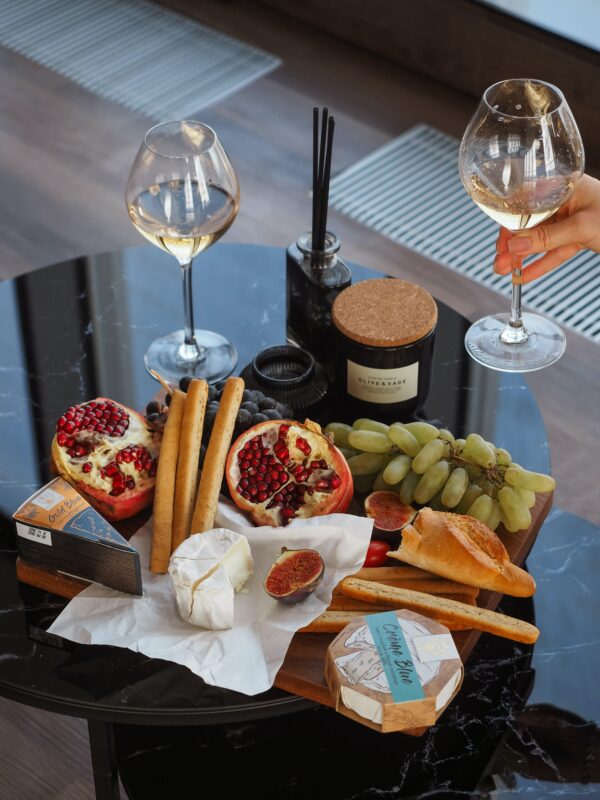Photograph of a charcuterie board with pomegranates, grapes, bread, and cheese on a black marble table