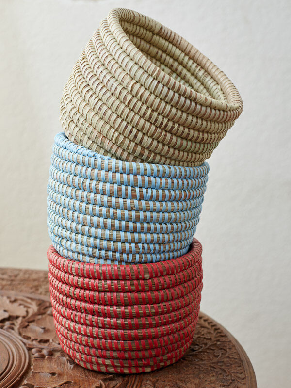 A stack of three mini woven plant baskets in natural, blue, and red fibers