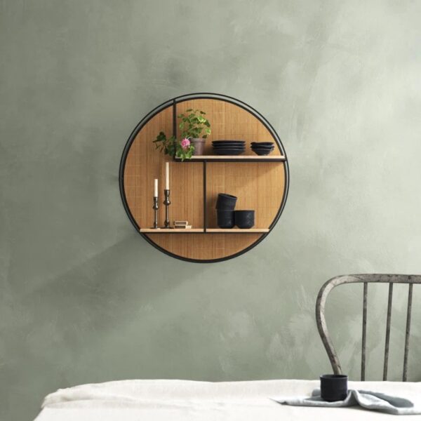 Photograph of a circle wall shelf on a green grey wall filled with black dishware, candles, and a potted plant