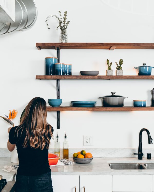 Open fixed bracket shelving for the kitchen with three tiers, filled with ceramic dishware and some potted plants for shelf decor