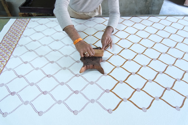 Photograph of an artisan using wood block printing to create a trellis pattern on fabric