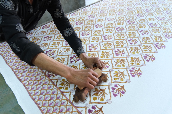 Photograph of artisan using wood block printing to create floral pattern on cotton fabric