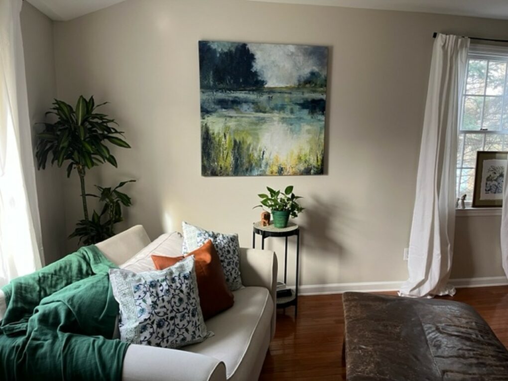 Photograph of neutral living room and green pops of color through pillow covers, art, and plants