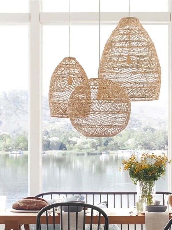 Photograph of three woven pendant lampshades hung above a dining table overlooking big window in front of a lake.